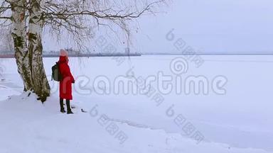 可爱的年轻女子站在白雪覆盖的河岸上的桦树附近，看着<strong>画报</strong>的风景